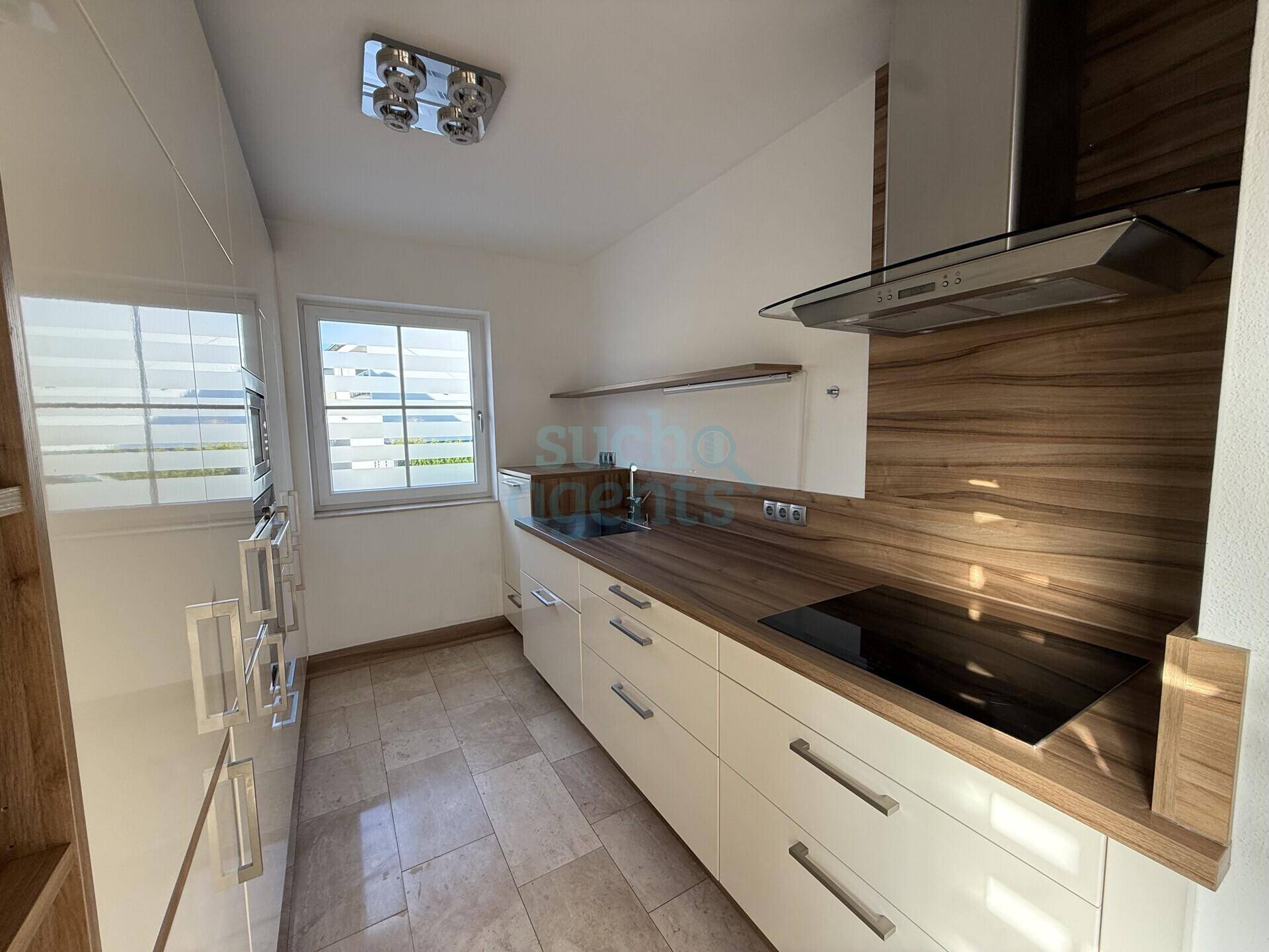 Moderne Einbauküche mit weißen Hochglanzfronten, Holzdetails und Induktionskochfeld.