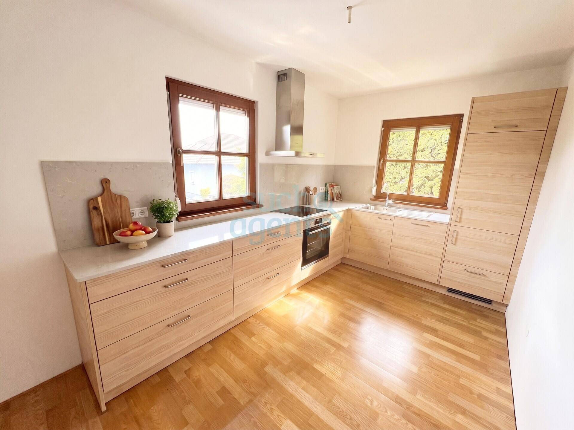 Moderne Einbauküche mit hellen Holzfronten, Stein-Arbeitsplatten und integrierten Geräten.