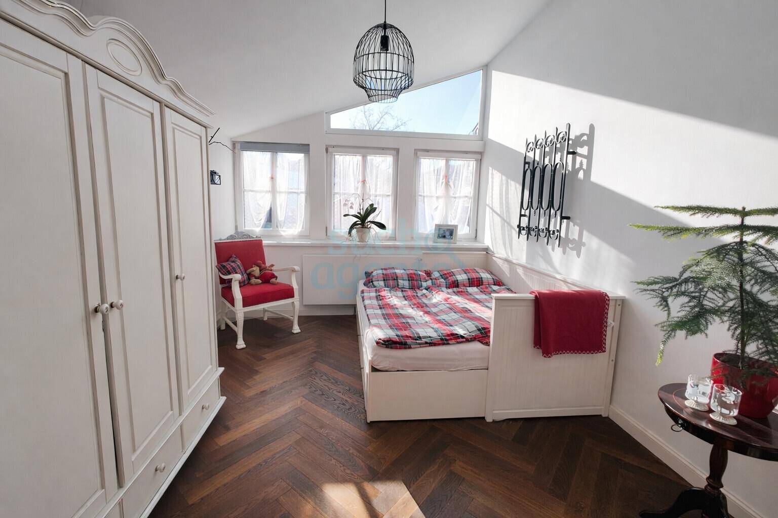 Ein helles Schlafzimmer mit schrägem Dach, Holzboden und einem gemütlichen Bett mit karierter Bettwäsche.