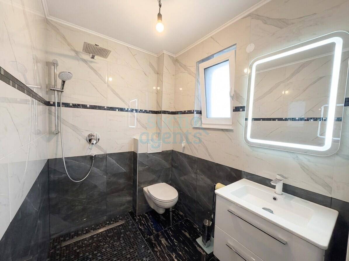 Modernes Badezimmer mit begehbarer Dusche, Wand-WC, beleuchtetem Spiegel und stilvollen Fliesen.