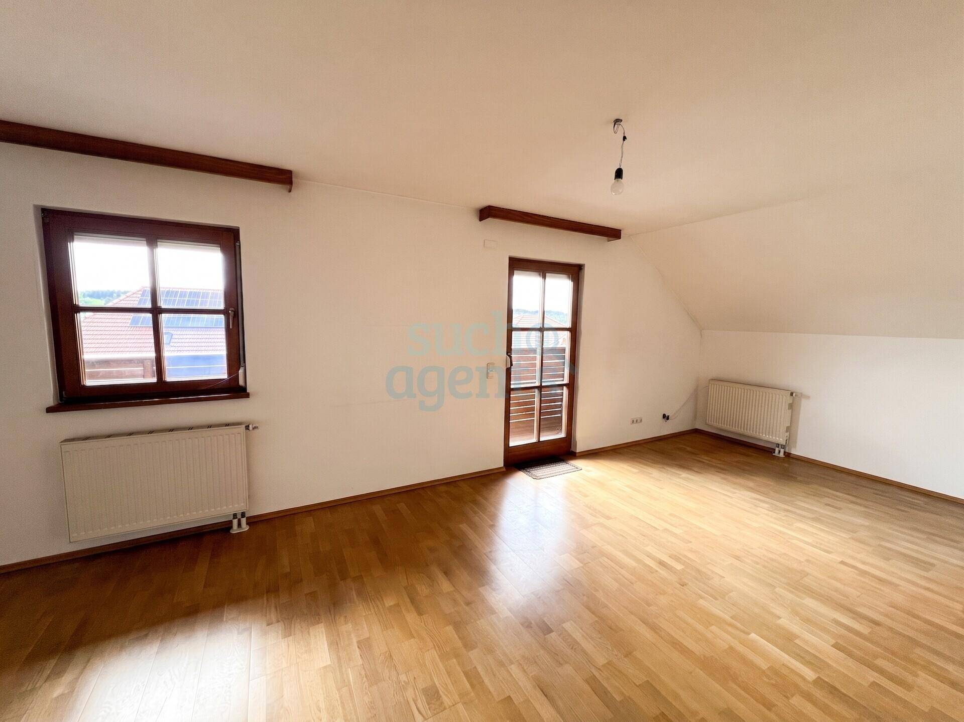 Geräumiges Zimmer im Dachgeschoss mit Holzbalken, Parkettboden und schrägen Wänden.