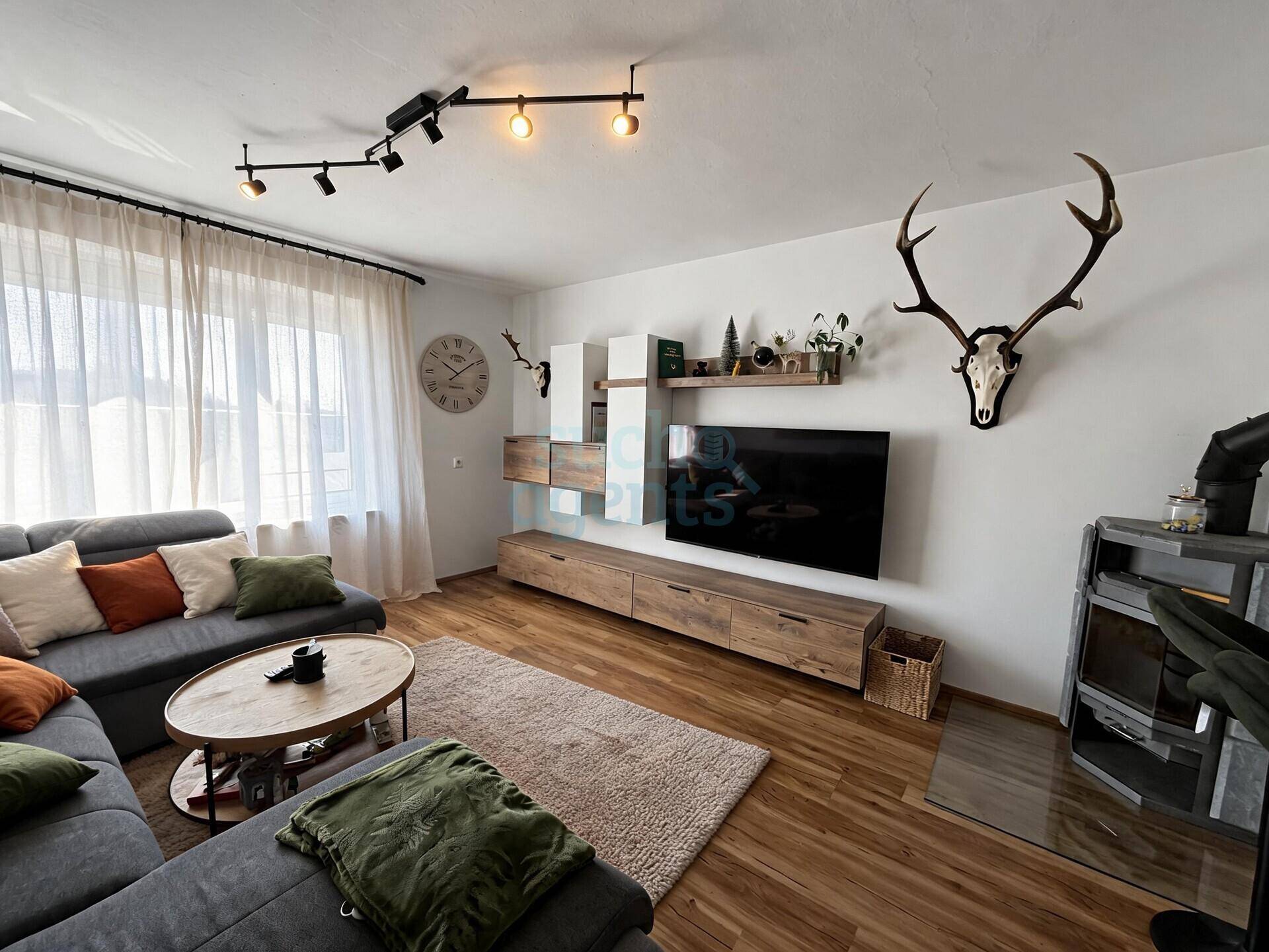 Gemütliches Wohnzimmer mit Holzboden, großem Sofa, TV-Möbel und Hirschgeweih-Dekoration an der Wand.