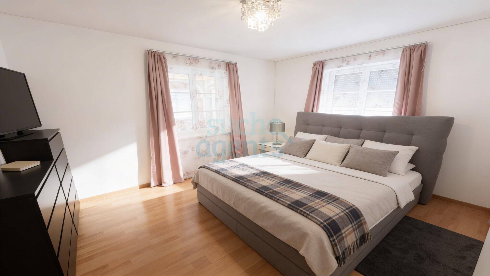 Helles Schlafzimmer mit Doppelbett, Holzfußboden und großen Fenstern mit Vorhängen.