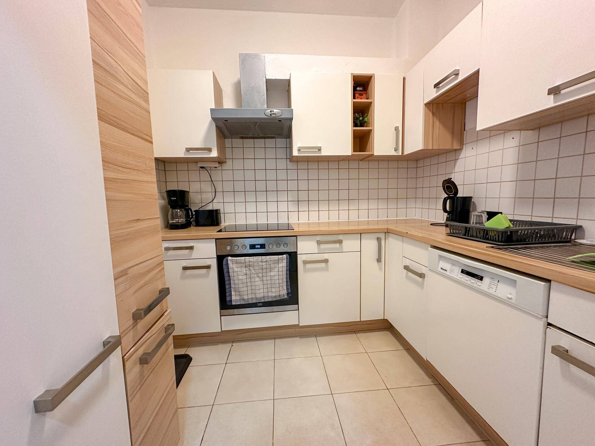 Helle Einbauküche mit weißen Fronten, Holz-Arbeitsplatten und Fliesenboden, ausgestattet mit modernen Geräten.