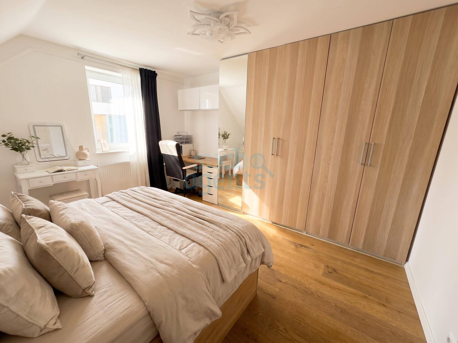 Helles Schlafzimmer mit Holzboden, großem Einbauschrank und Schreibtisch am Fenster.