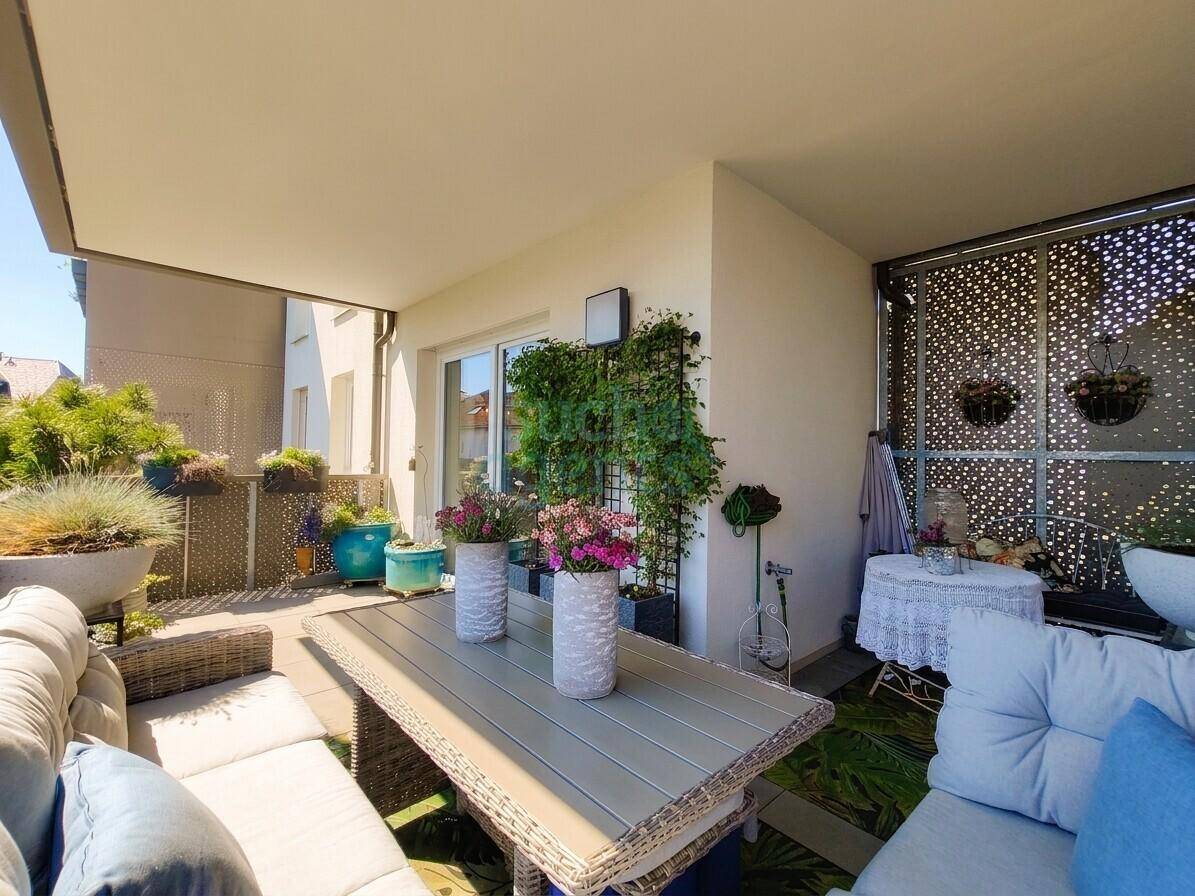 Sonnige Terrasse mit bequemen Outdoor-Möbeln, Pflanzen und einem dekorativen Sichtschutz.
