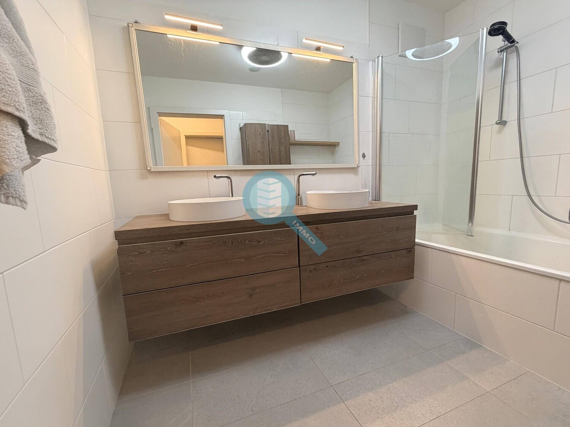 Modernes Badezimmer mit Doppelwaschbecken, großem Spiegel und Badewanne mit Duschfunktion.