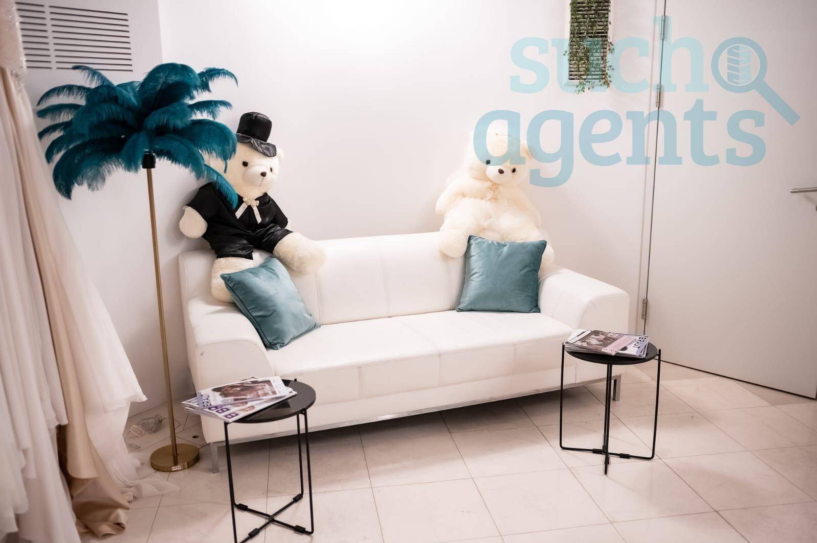 Gemütliche Sitzecke in einem Brautmodengeschäft mit weißem Sofa, Beistelltischen und dekorativen Elementen.