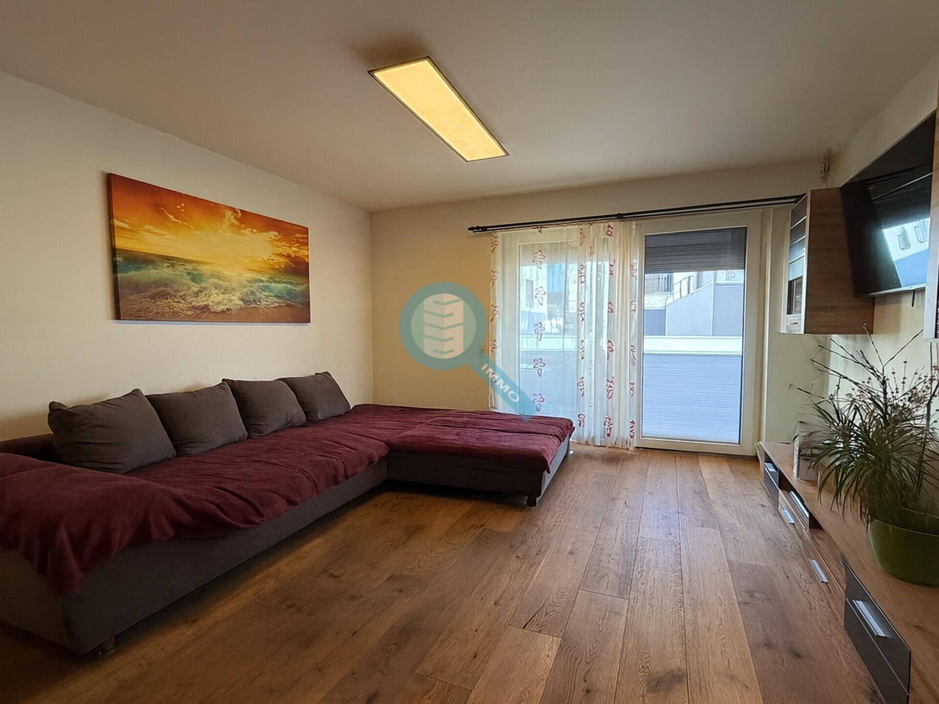 Helles Wohnzimmer mit Holzboden, großem Sofa und Zugang zu einem Balkon oder einer Terrasse.