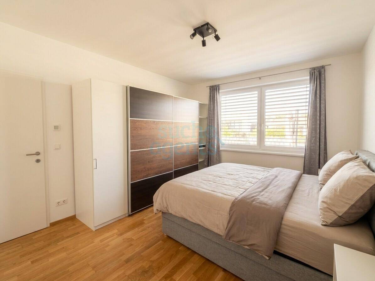 Helles Schlafzimmer mit Holzboden, großem Kleiderschrank und Fenster mit Jalousien.