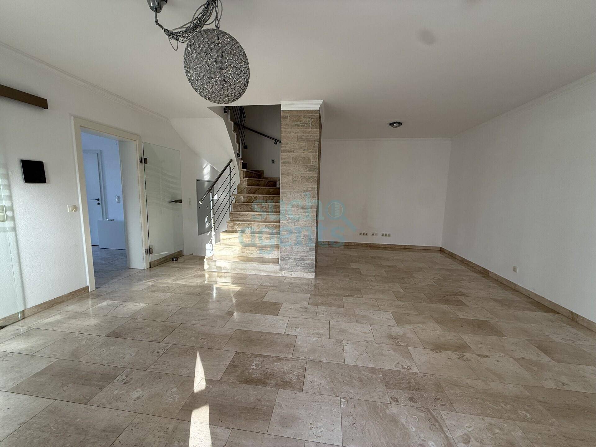 Geräumiges, helles Wohnzimmer mit großformatigen Fliesen und offener Treppe.