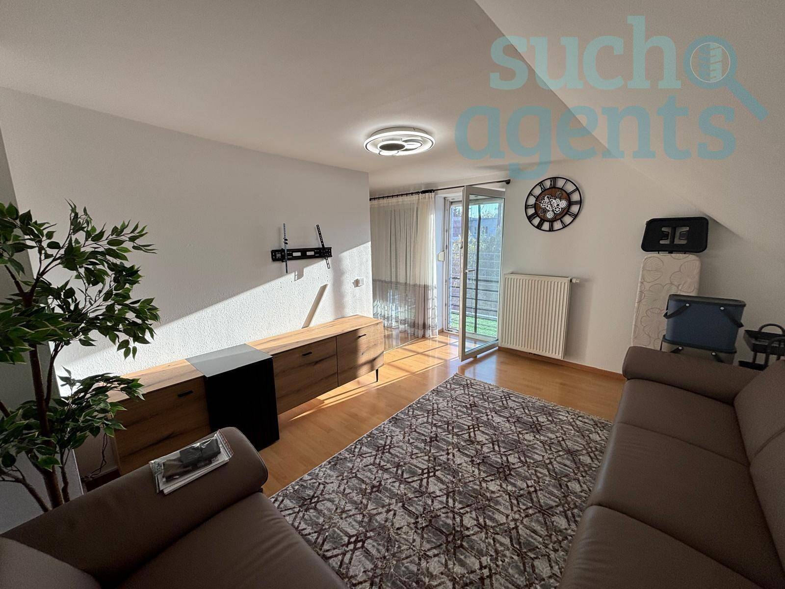 Helles Wohnzimmer mit Holzboden, Zugang zum Balkon und moderner Deckenleuchte.