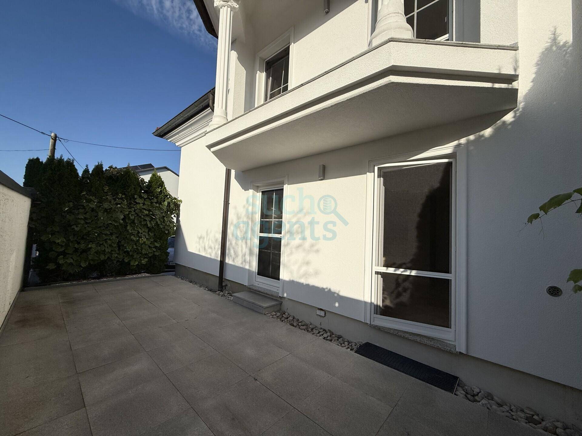 Seitenansicht des Hauses mit gepflastertem Bereich und Zugangstür.