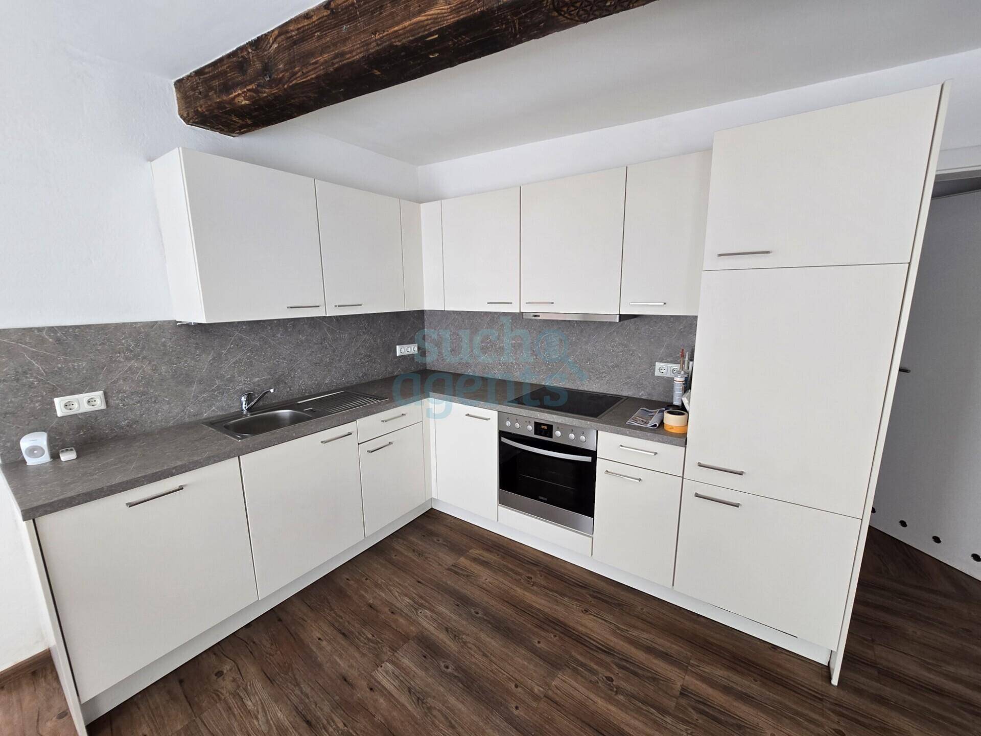 Funktionale Einbauküche mit weißen Schränken, dunkler Arbeitsplatte und Holzbalken an der Decke.