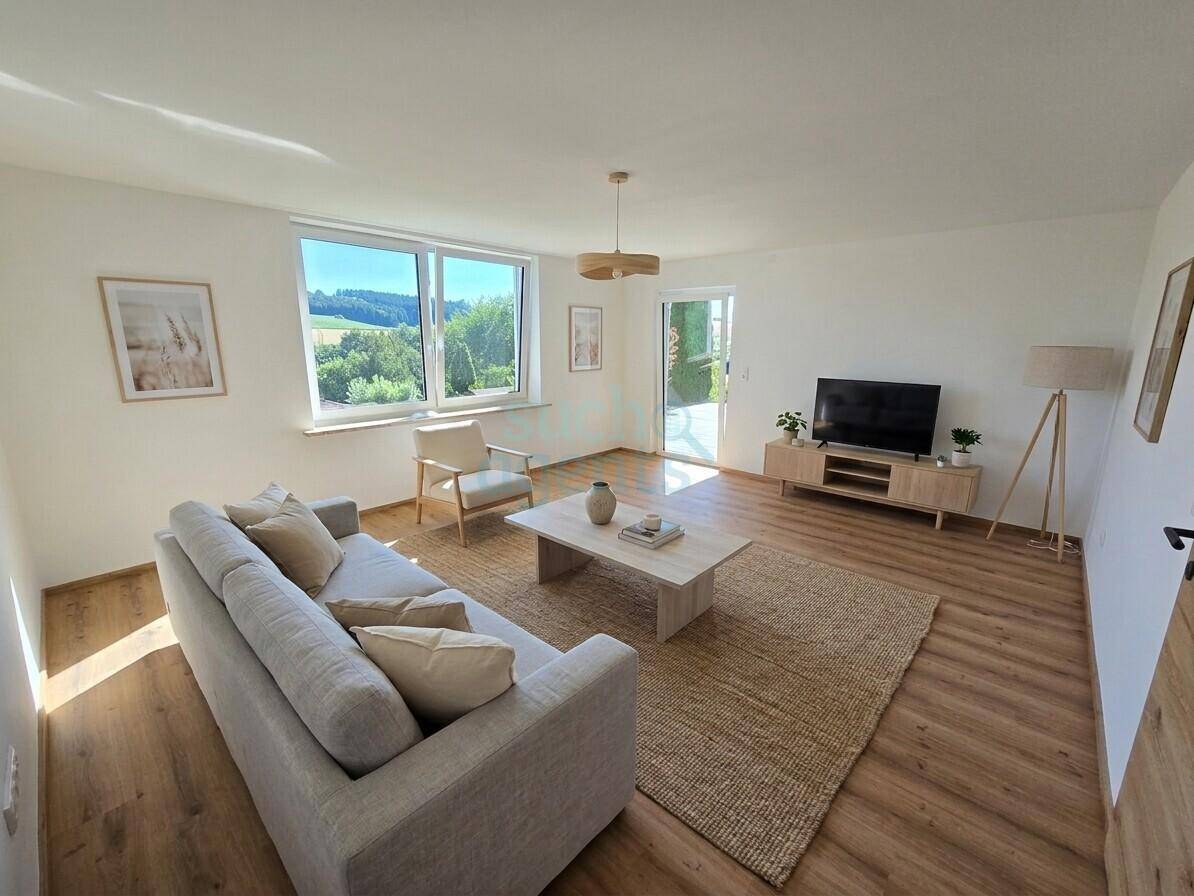 Helles Wohnzimmer mit modernem Interieur, Laminatboden und großen Fenstern mit Blick ins Grüne.