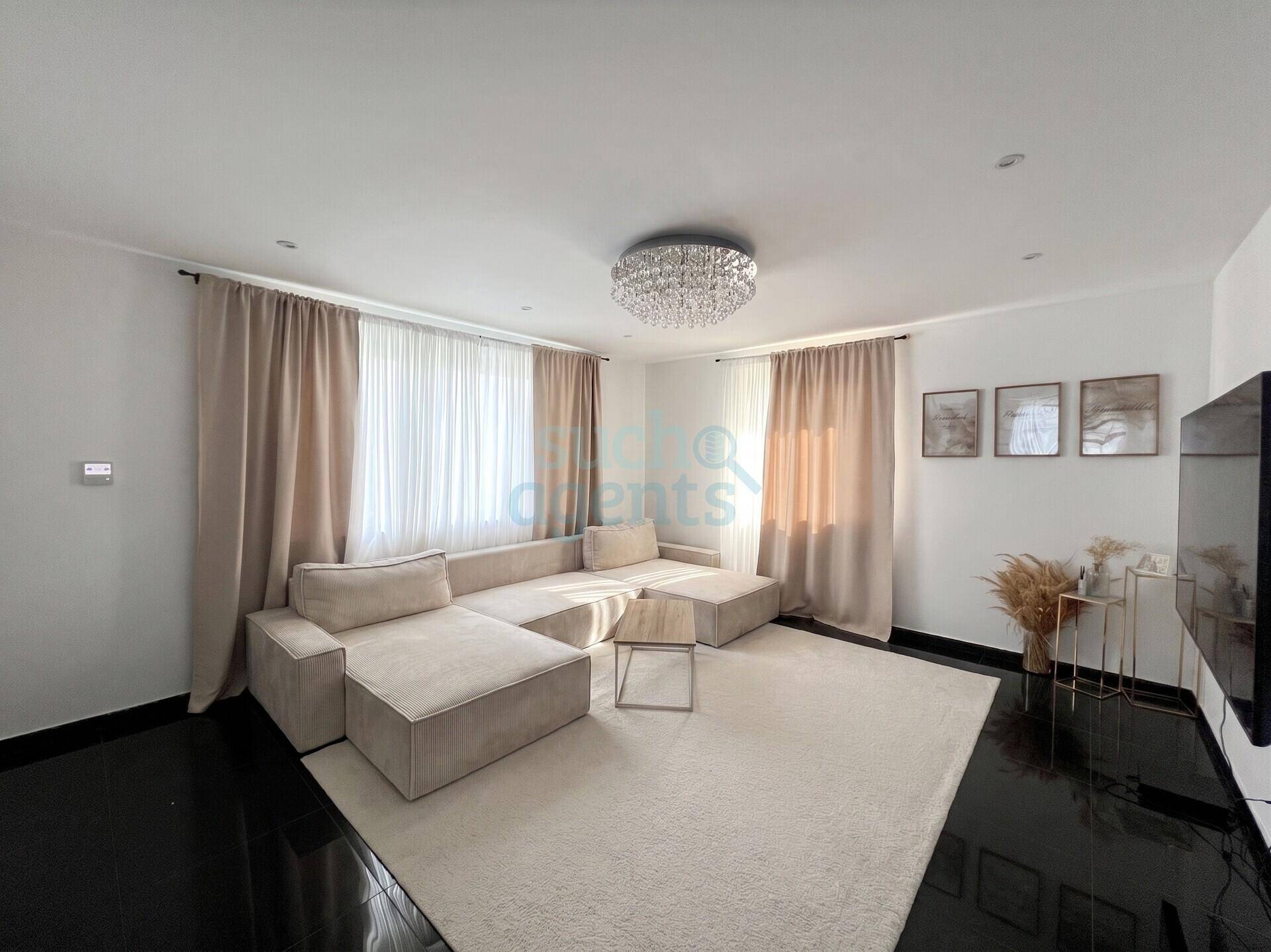Gemütliches Wohnzimmer mit großem Ecksofa, hellem Teppich und elegantem Kronleuchter.