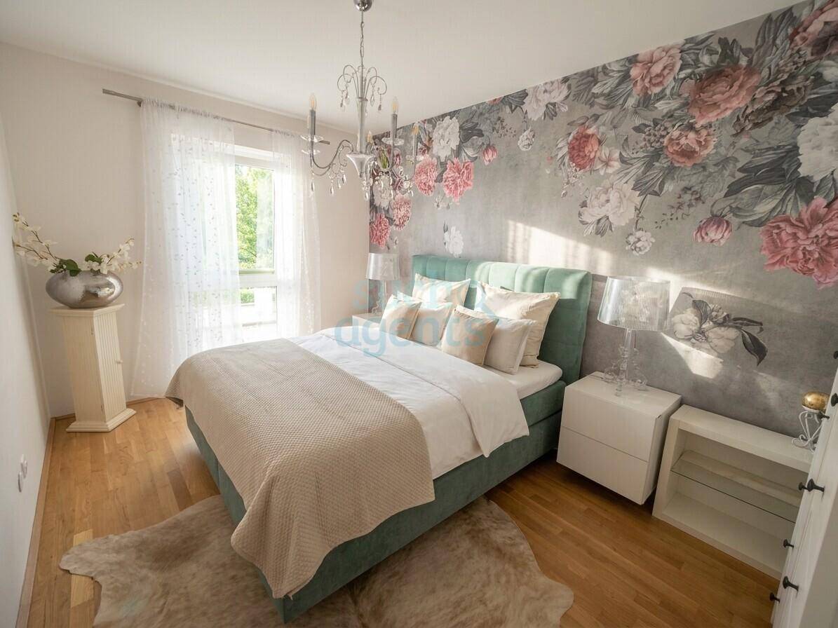 Gemütliches Schlafzimmer mit auffälliger floraler Tapete, Holzboden und viel Tageslicht.