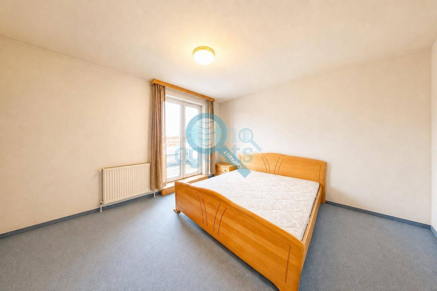Schlafzimmer mit Doppelbett, blauem Teppichboden und Zugang zum Balkon.
