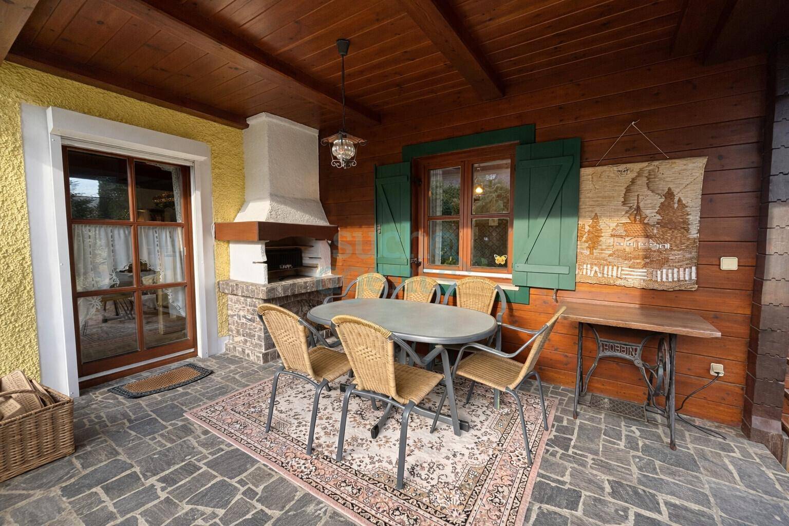 Überdachte Terrasse mit Steinfliesen, Essbereich und eingebautem Grill, ideal für gesellige Stunden im Freien.