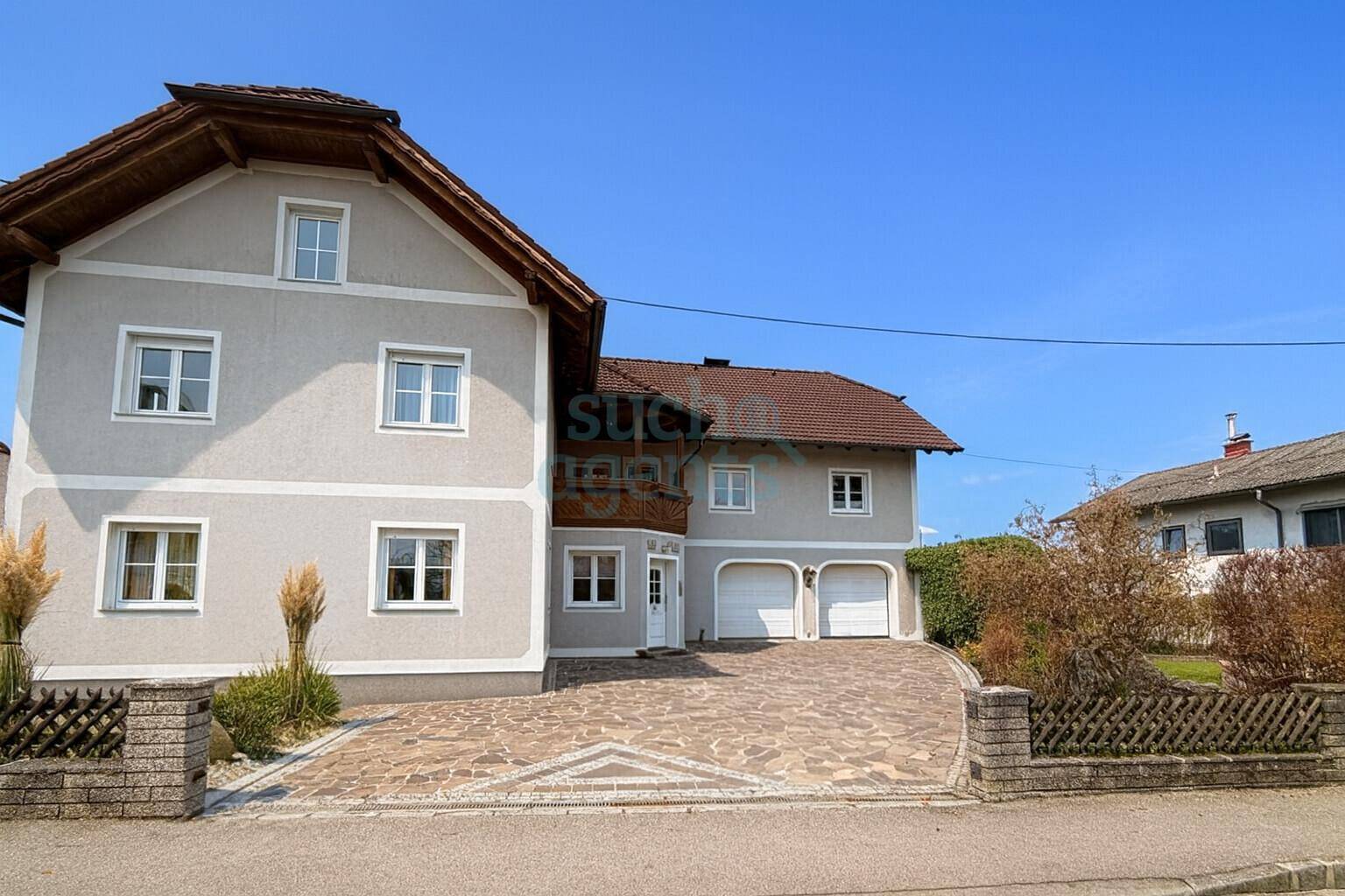 Gut erhaltenes Einfamilienhaus mit heller Fassade, gepflasterter Auffahrt und integrierten Garagen.