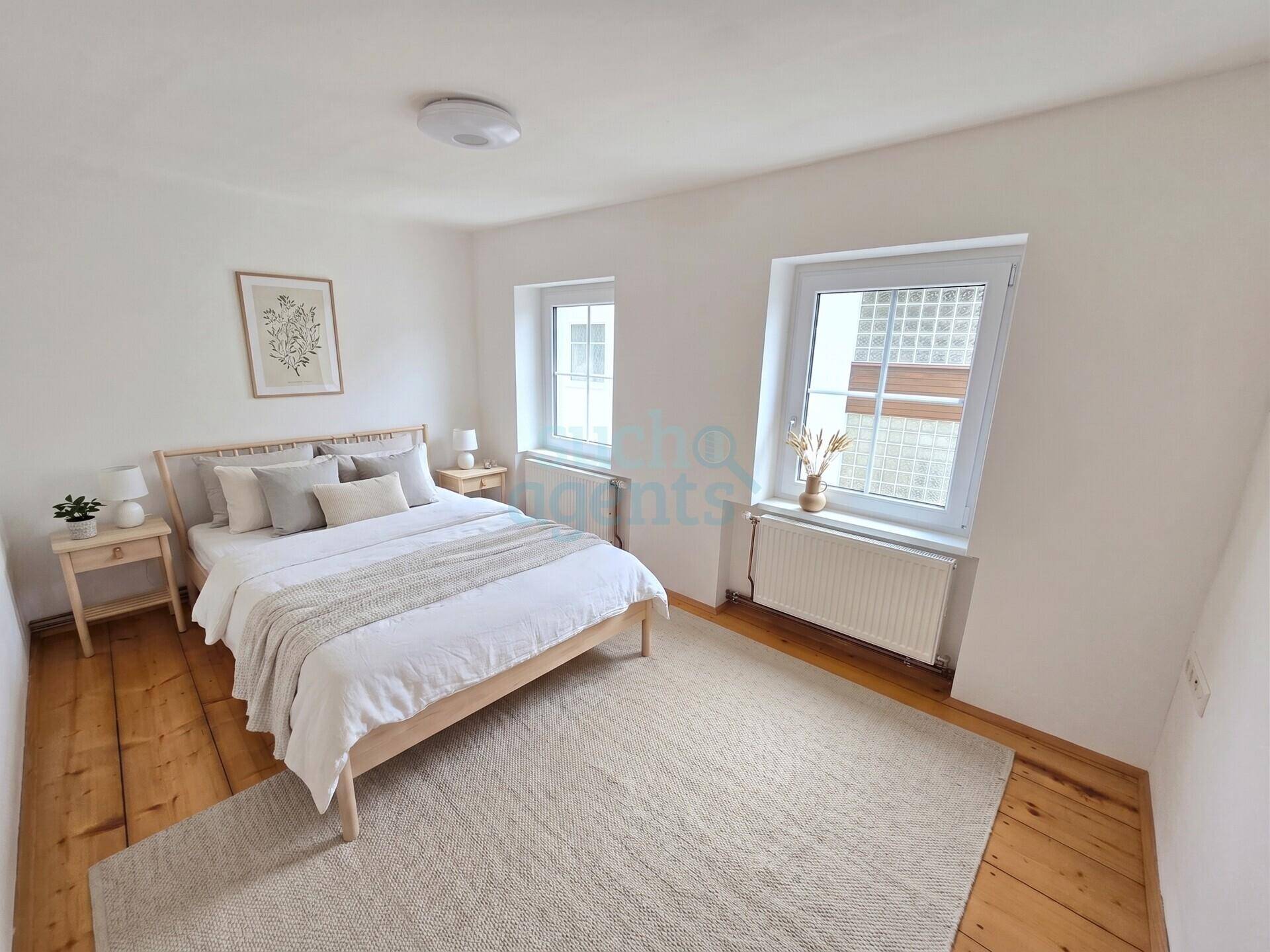 Helles Schlafzimmer mit Holzdielenboden, Doppelbett und zwei Fenstern für viel Tageslicht.