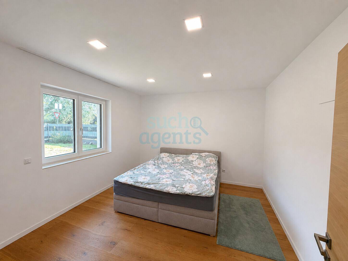 Helles Schlafzimmer mit Holzboden und Blick ins Grüne durch das Fenster.