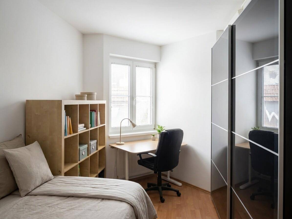 Helles Schlafzimmer mit Bett, Schreibtisch, Bücherregal und großem Kleiderschrank.