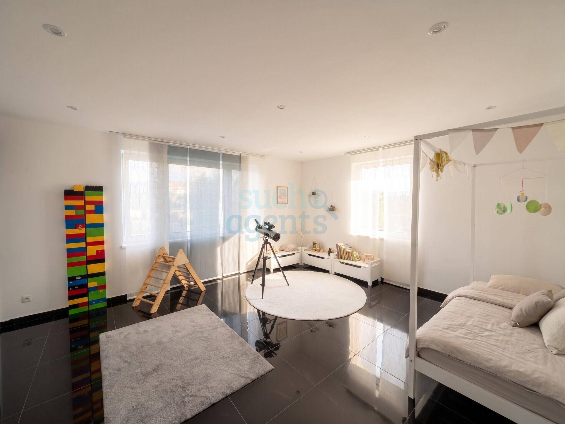 Helles Kinderzimmer mit Spielbereich, großem Fenster und dunklem Fliesenboden.