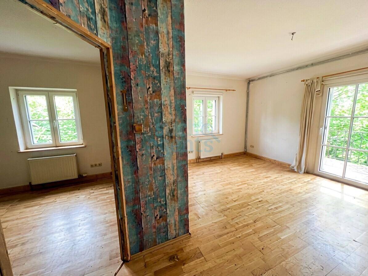 Heller Raum mit Holzboden, einer farbigen Akzentwand und Zugang zu einem Balkon.