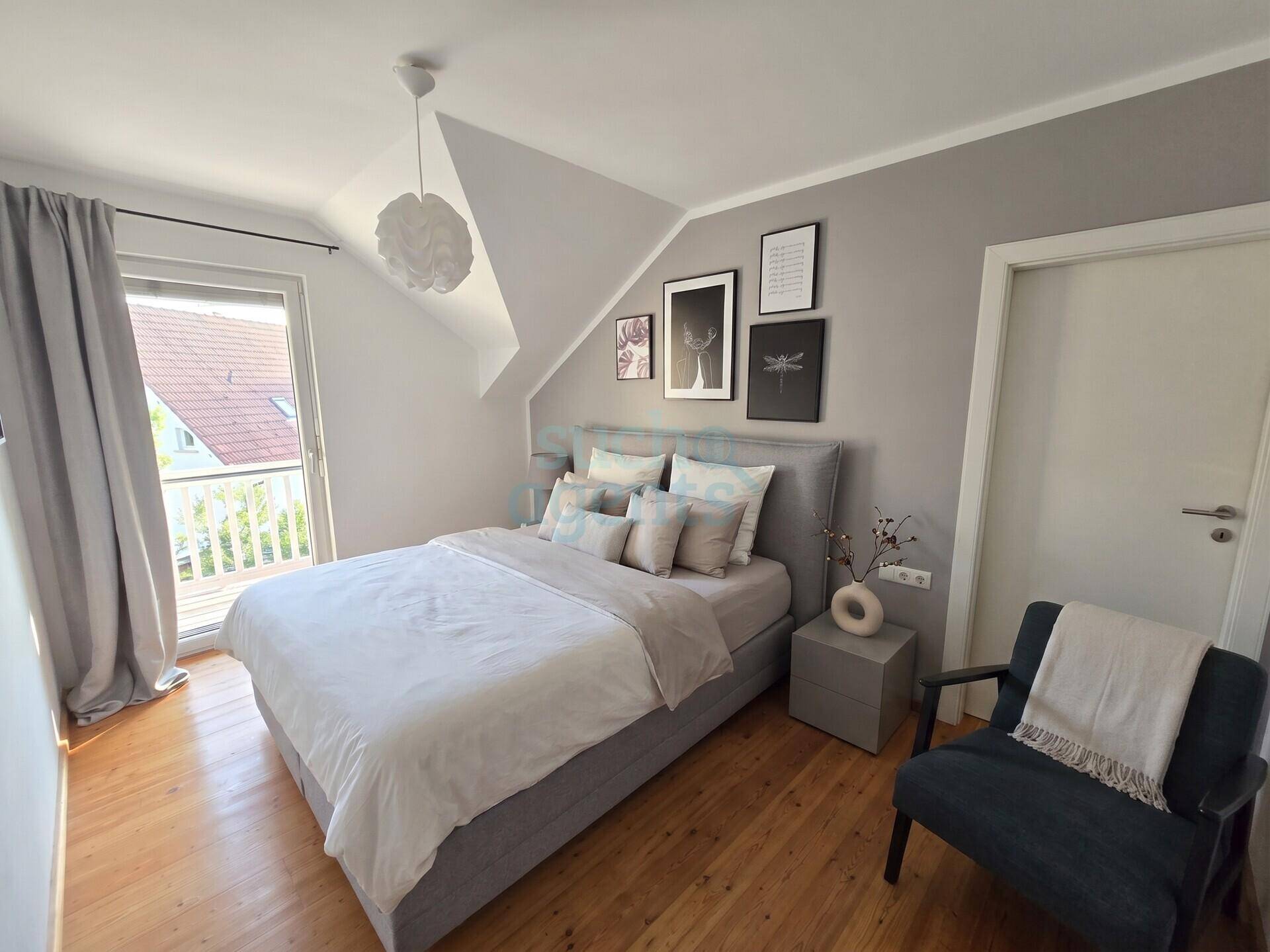 Helles Schlafzimmer mit Doppelbett, Holzboden und Zugang zu einem kleinen Balkon, unter einer Dachschräge.