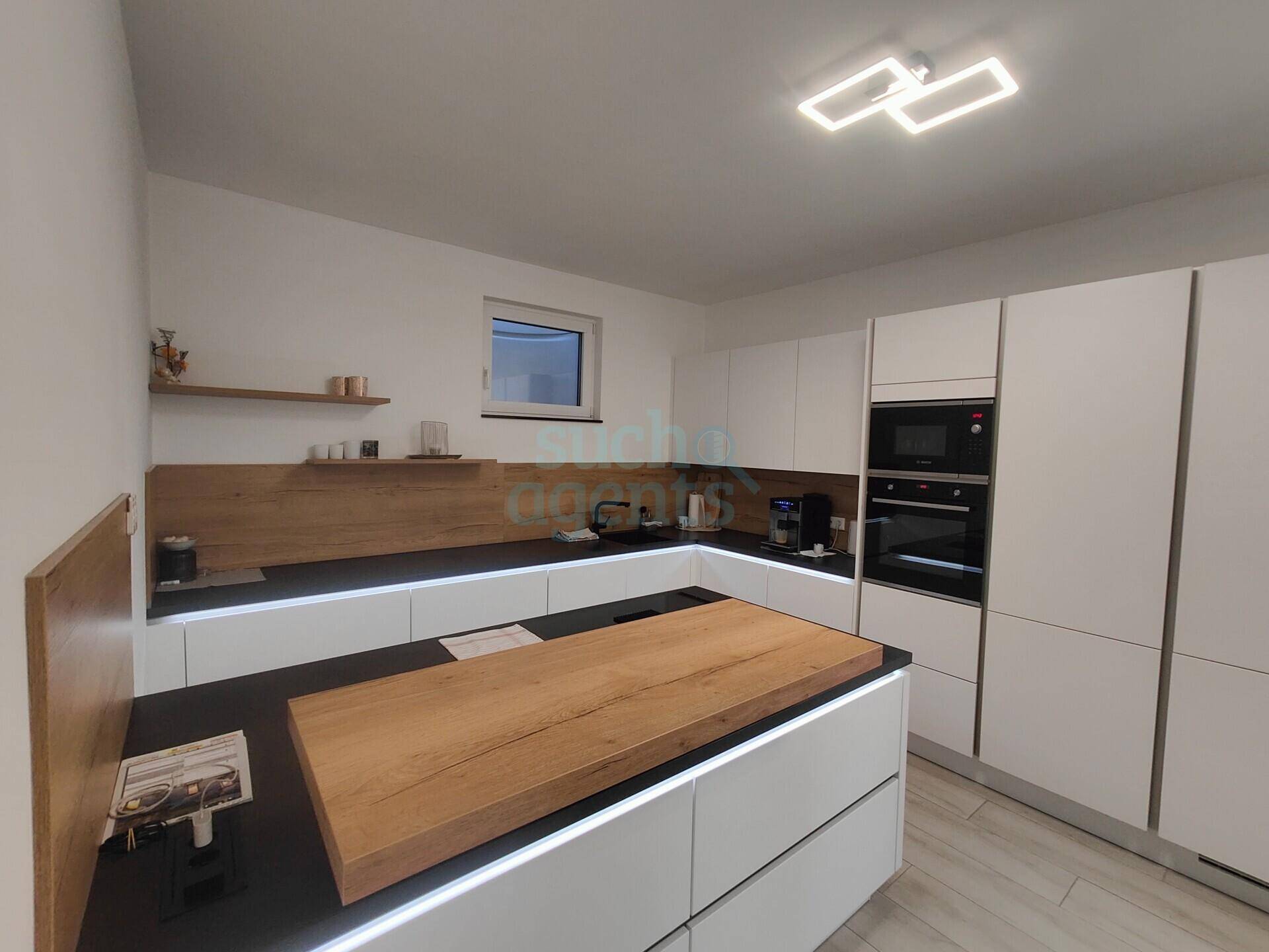 Moderne Einbauküche mit weißen Fronten, Holzarbeitsplatte auf der Insel und integrierten Geräten.