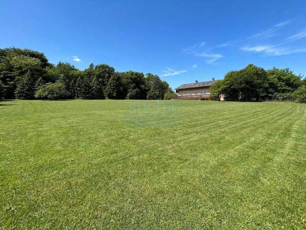 Weitläufige Grünfläche mit gepflegtem Rasen und einem Wohnhaus im Hintergrund unter blauem Himmel.