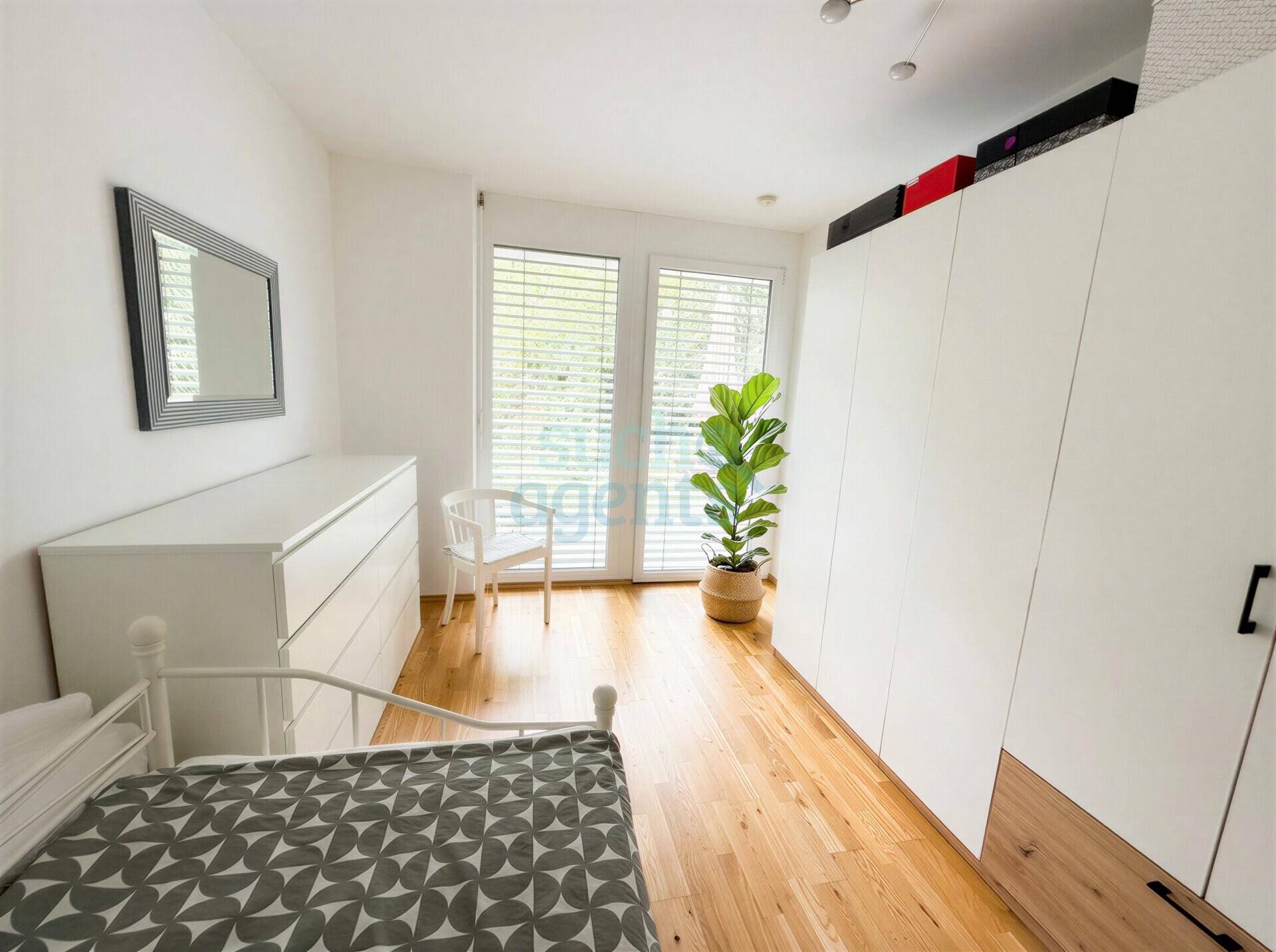 Helles Schlafzimmer mit Holzboden, großem Kleiderschrank und viel Tageslicht durch die Fenster.