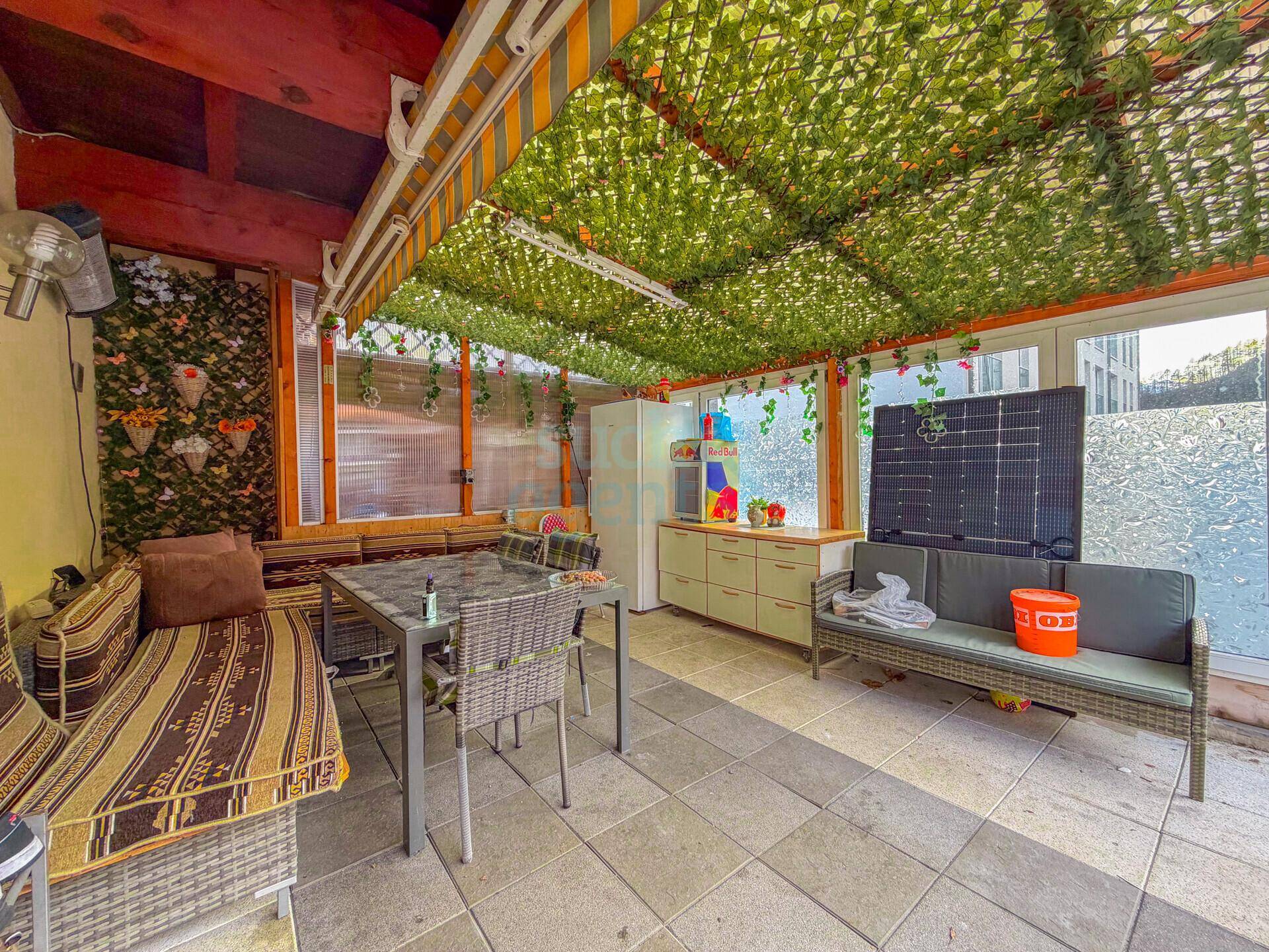 Überdachte Terrasse mit Sitzgelegenheiten, Esstisch und grüner Dekoration für entspannte Stunden.