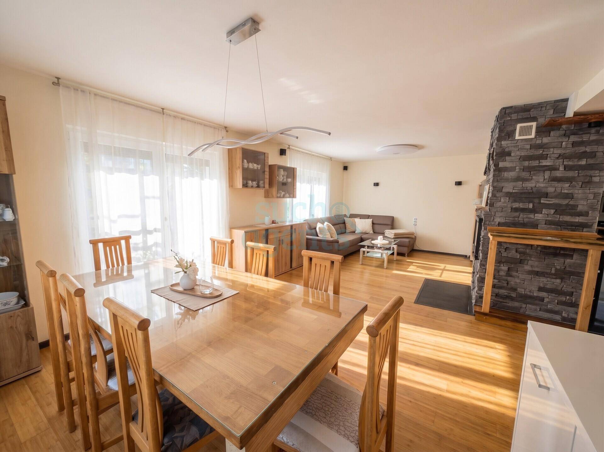 Geräumiger Wohn-Essbereich mit Holzboden, großem Esstisch und Kamin mit Steinverkleidung.