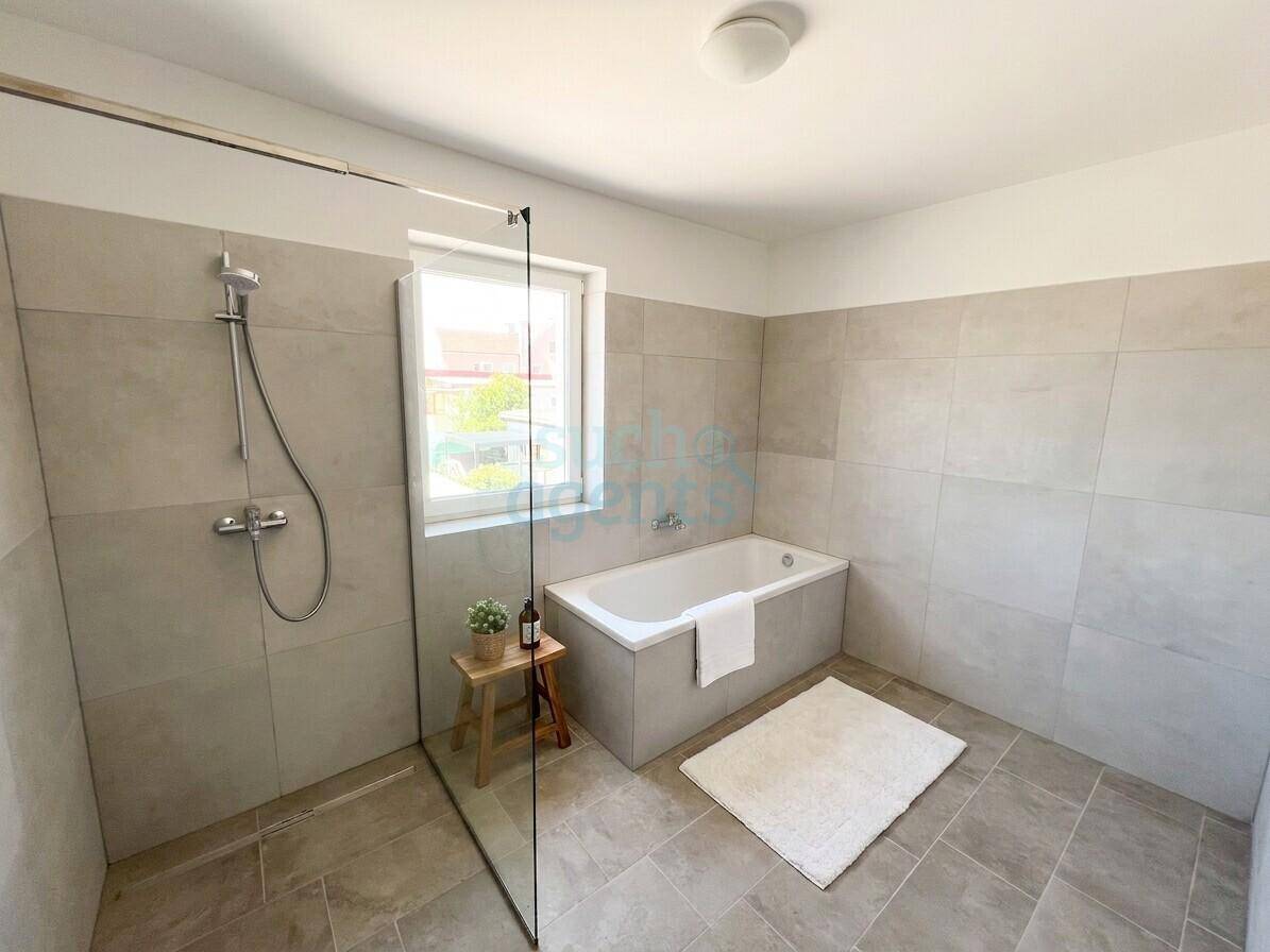 Modernes Badezimmer mit Dusche, Badewanne und hellgrauen Fliesen an Wänden und Boden.