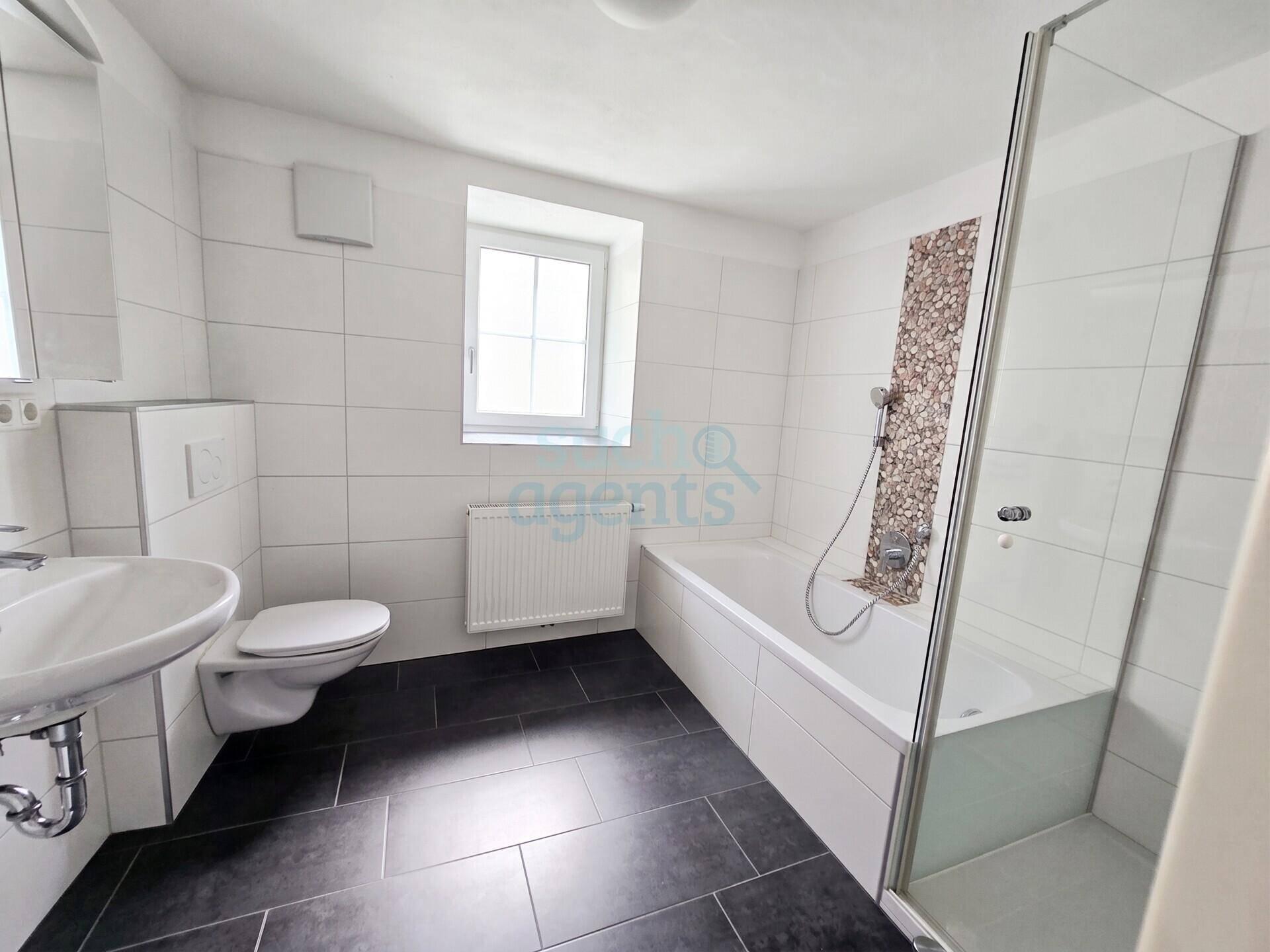 Modernes Badezimmer mit Badewanne, Duschkabine, WC und Fenster für natürliche Belüftung.