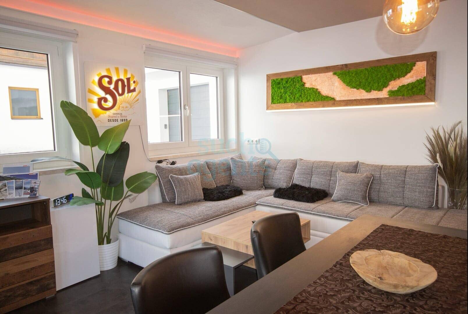 Gemütlicher Wohnbereich mit Ecksofa, Holztisch und dekorativer Mooswand.