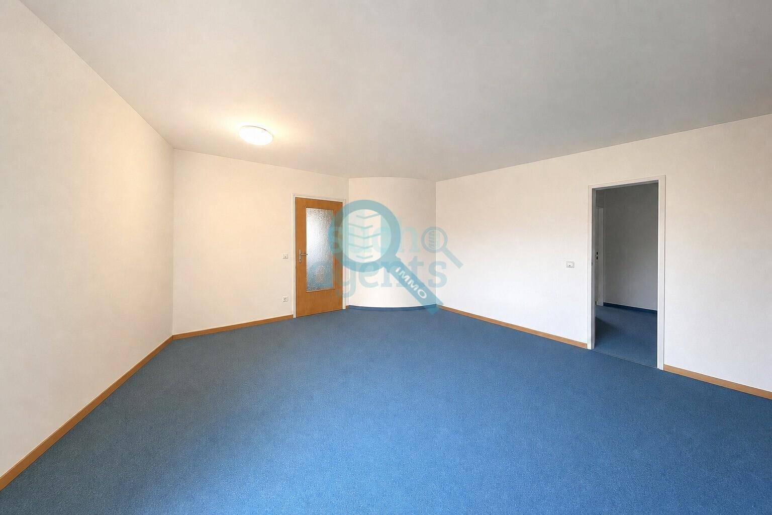 Helles, leeres Zimmer mit blauem Teppichboden und weiß gestrichenen Wänden.