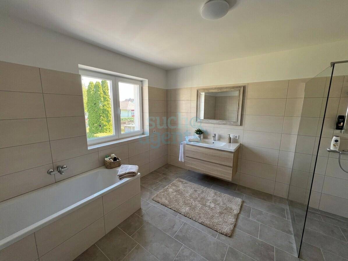 Modernes Badezimmer mit beigen Fliesen, Badewanne, begehbarer Dusche und Fenster.
