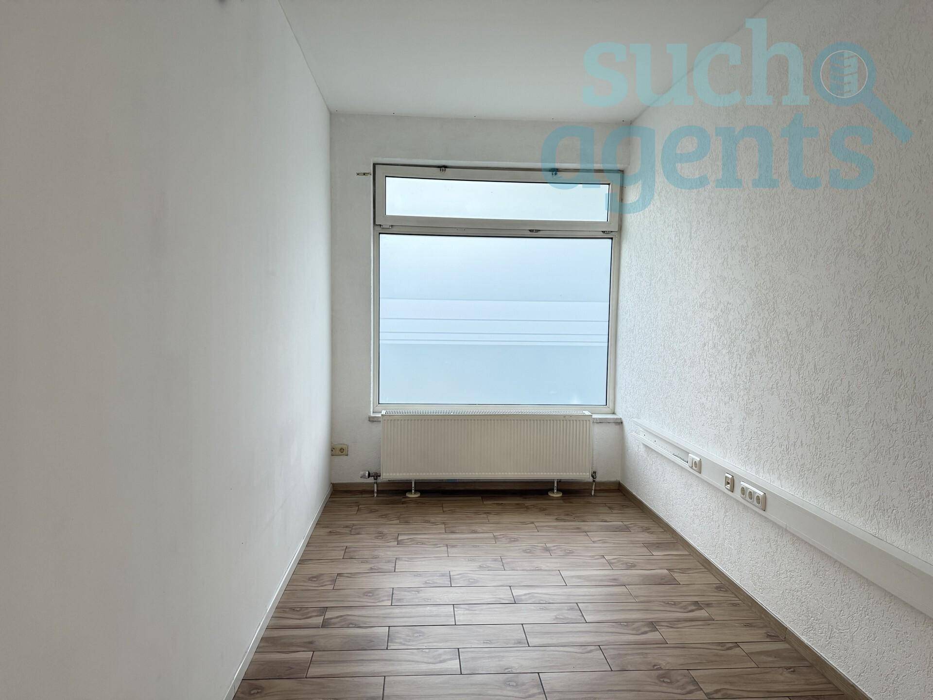 Leerer Raum mit großem Fenster, Heizkörper und Holzbodenoptik.