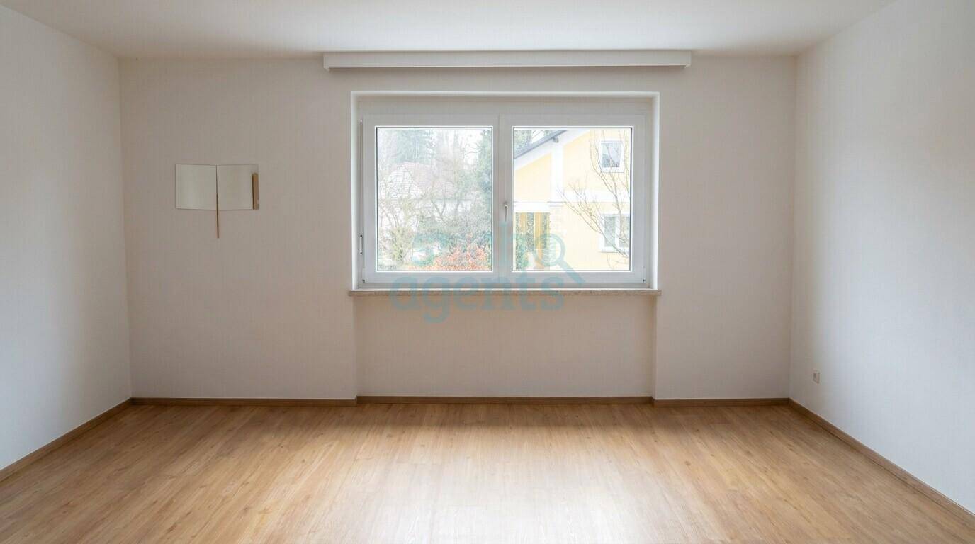Leerer Raum mit hellem Holzfußboden und einem großen Fenster, das viel Tageslicht hereinlässt.