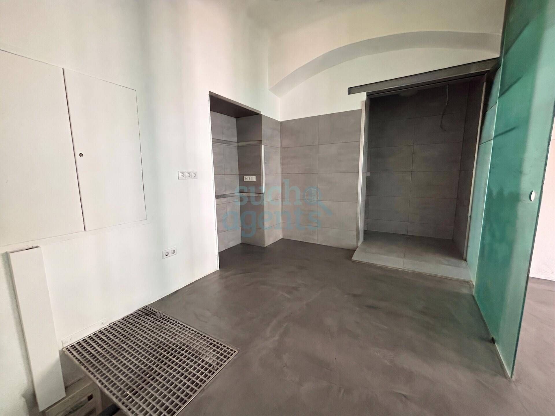 Badezimmer mit modernem Betonboden, grauen Fliesenwänden und einer offenen Duschkabine.