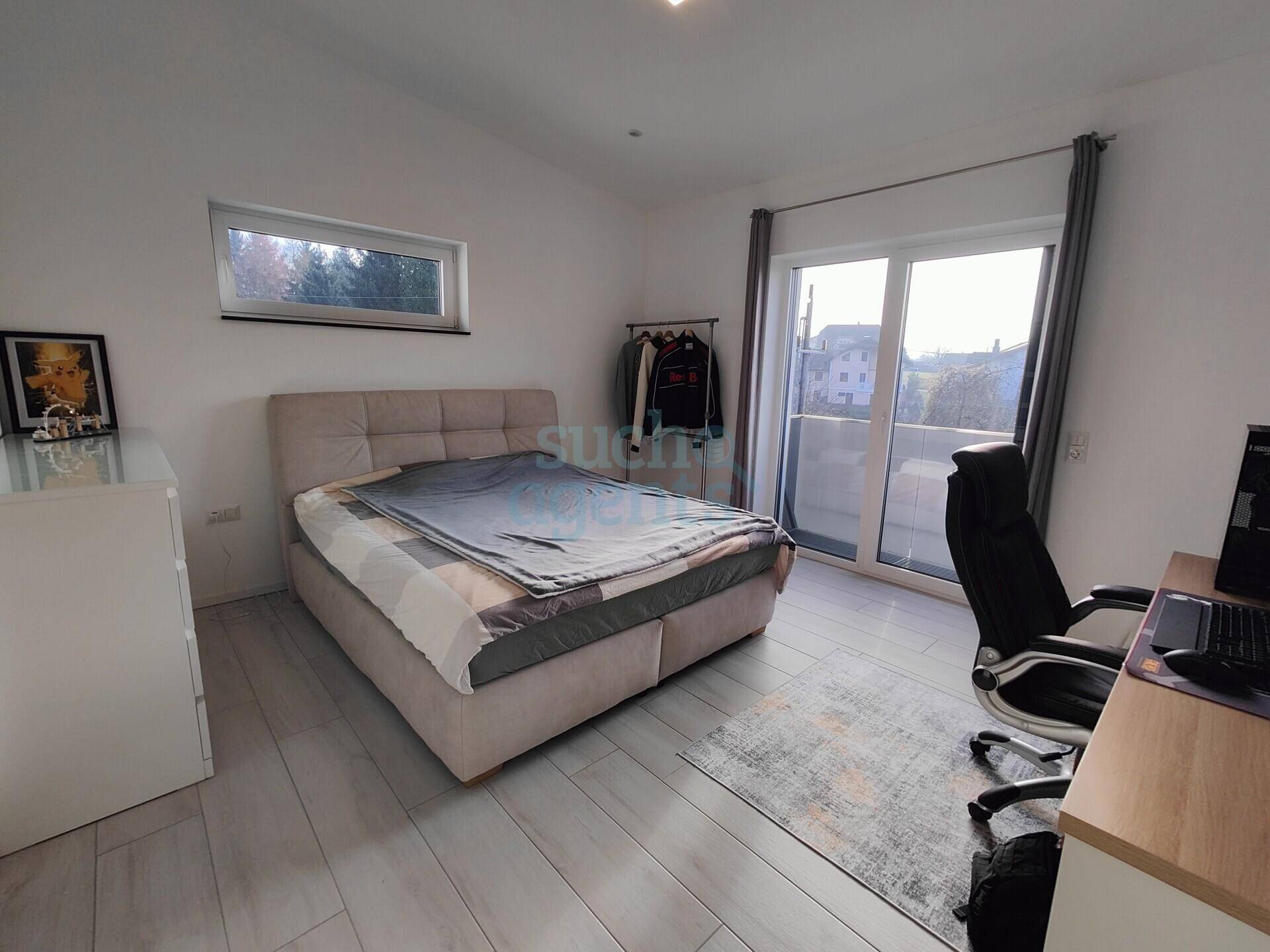 Modernes Schlafzimmer mit Doppelbett, Schreibtisch und Zugang zu einem kleinen Balkon.