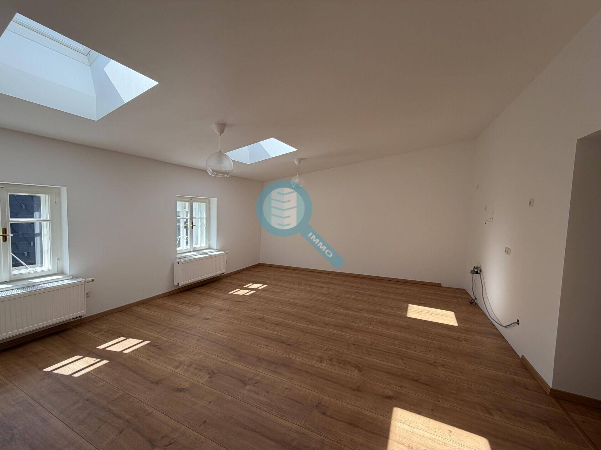 Heller Wohnraum mit Holzboden, weißen Wänden und zwei Dachfenstern für viel Tageslicht.