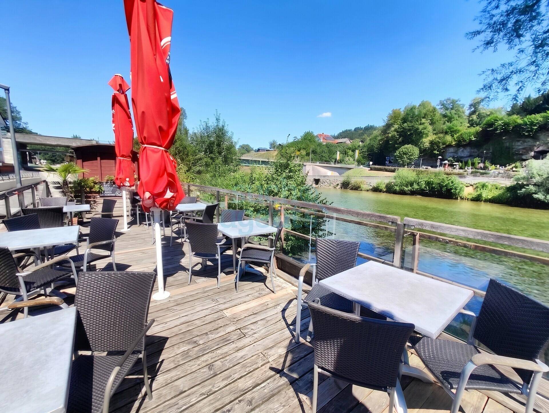 Sonnige Holzterrasse mit roten Sonnenschirmen und direktem Blick auf den Fluss oder See.