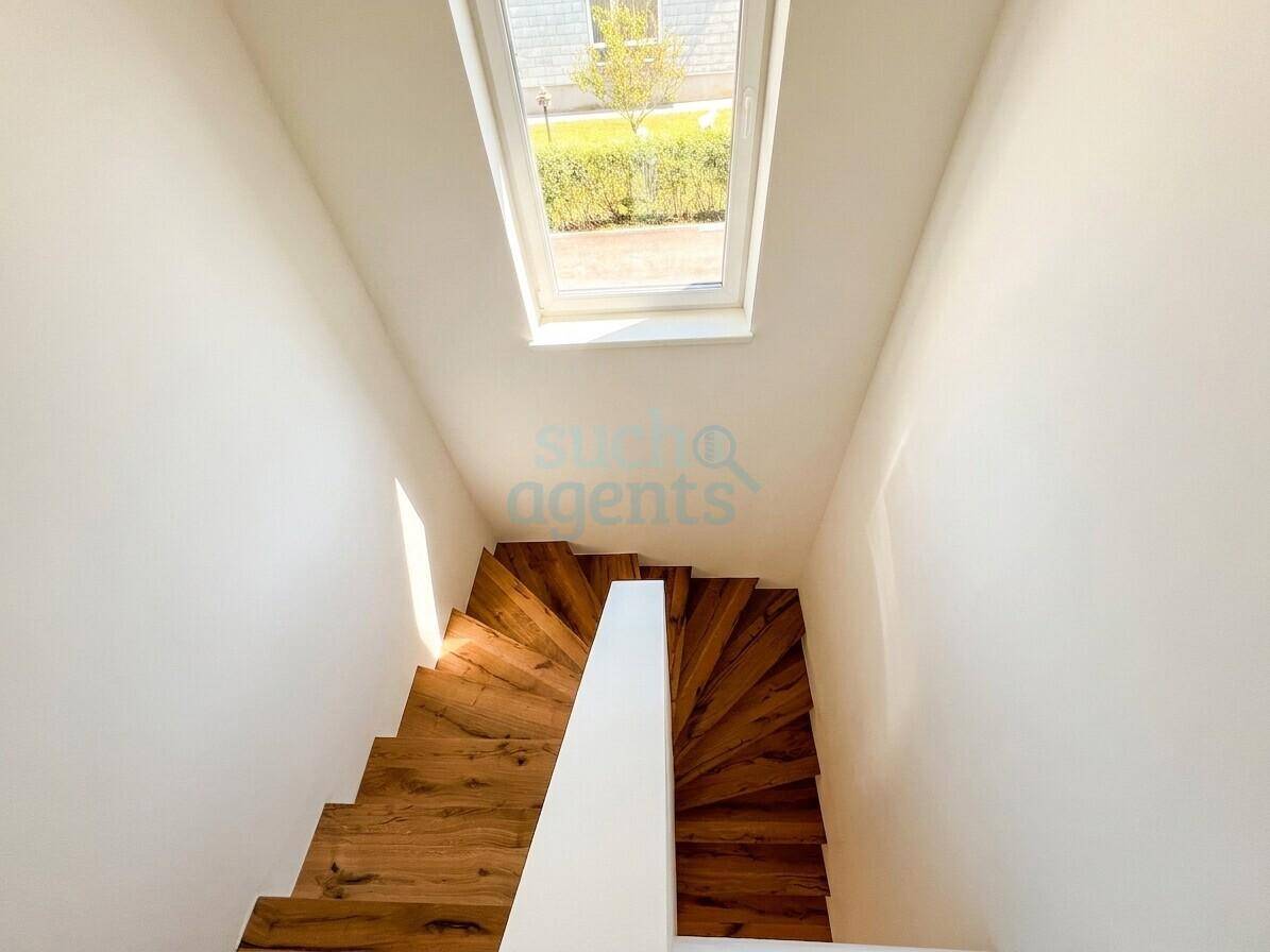 Heller Treppenaufgang mit Holzstufen und einem Dachfenster für natürliches Licht.