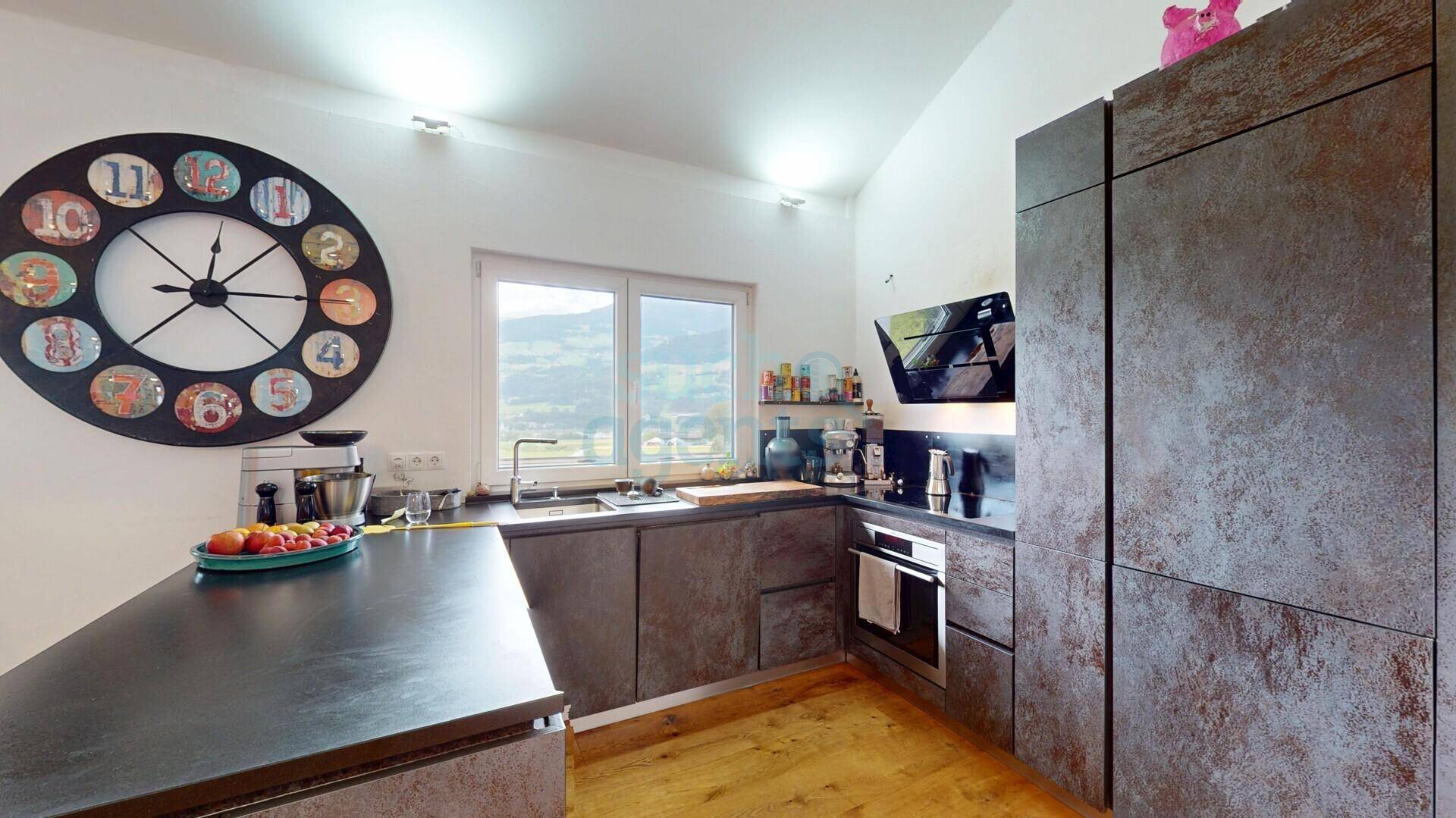 Moderne Küche mit dunklen Fronten, integrierten Geräten und Fenster mit Blick ins Grüne.