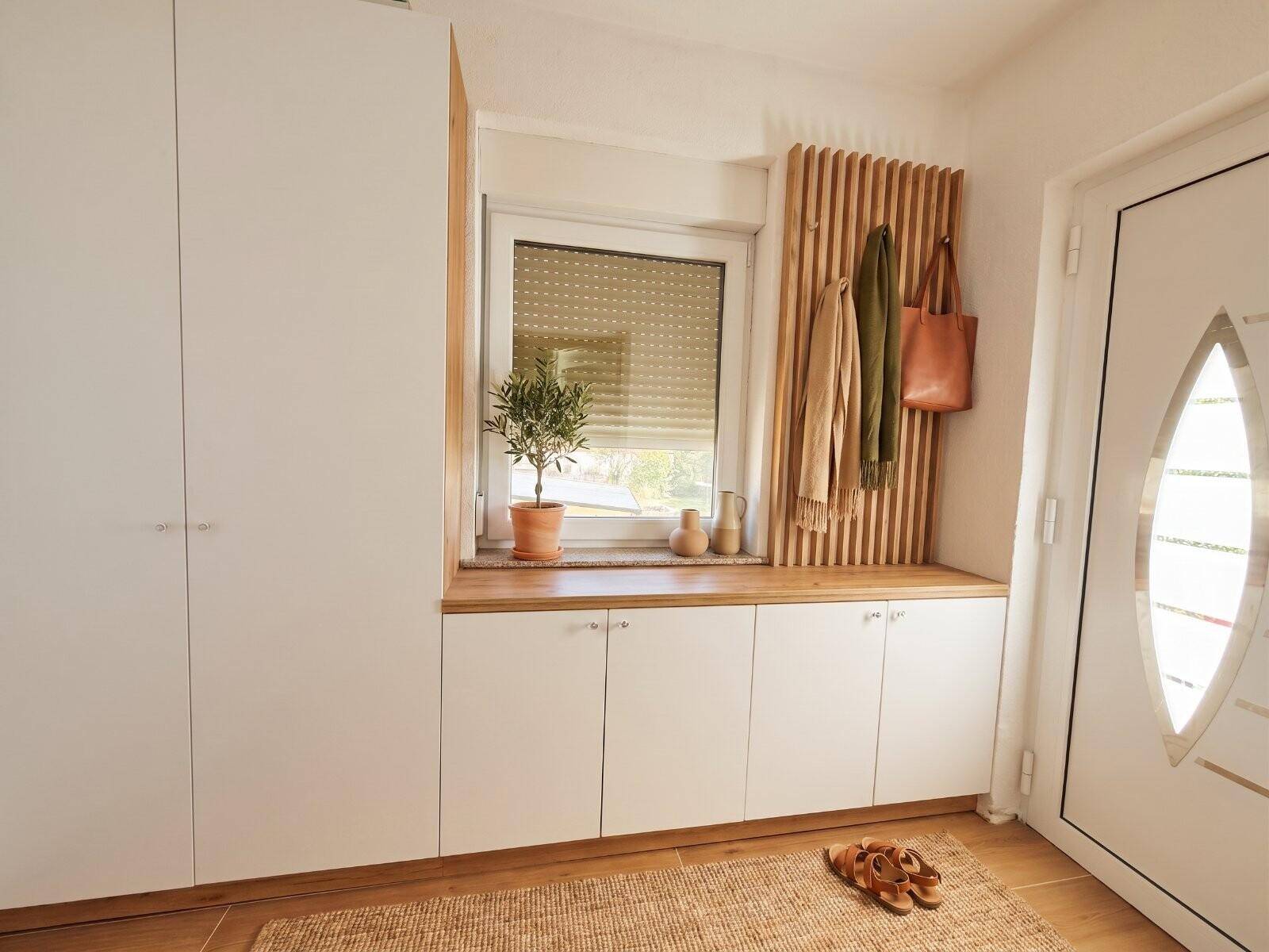 Heller Eingangsbereich mit Einbauschränken, Sitzbank und Garderobe aus Holz in modernem Design.
