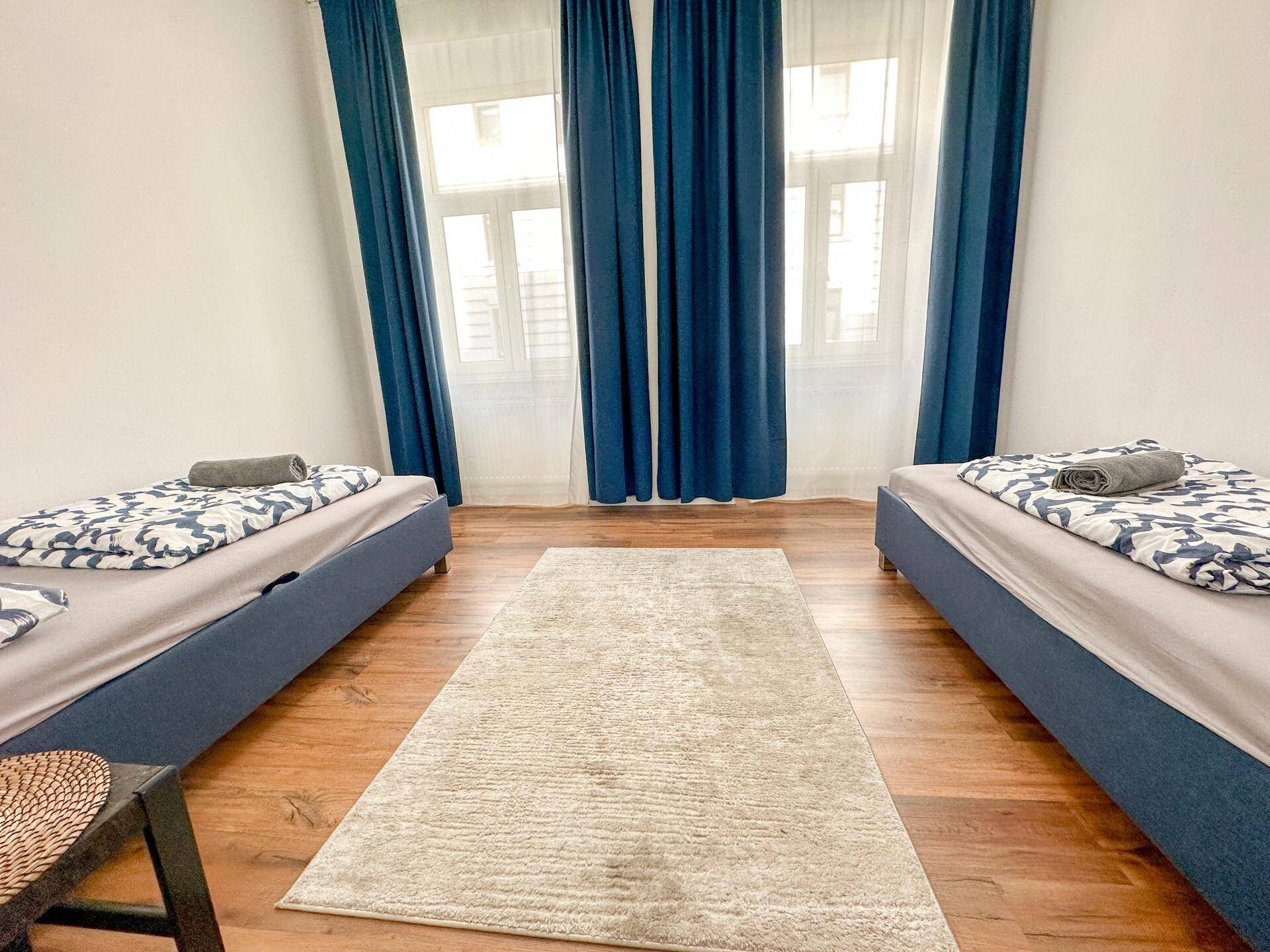 Schlafzimmer mit zwei Einzelbetten, blauen Vorhängen und hellem Holzfußboden.